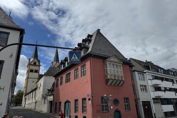 Red historic building with a church tower behind it under a cloudy sky in Koblenz.