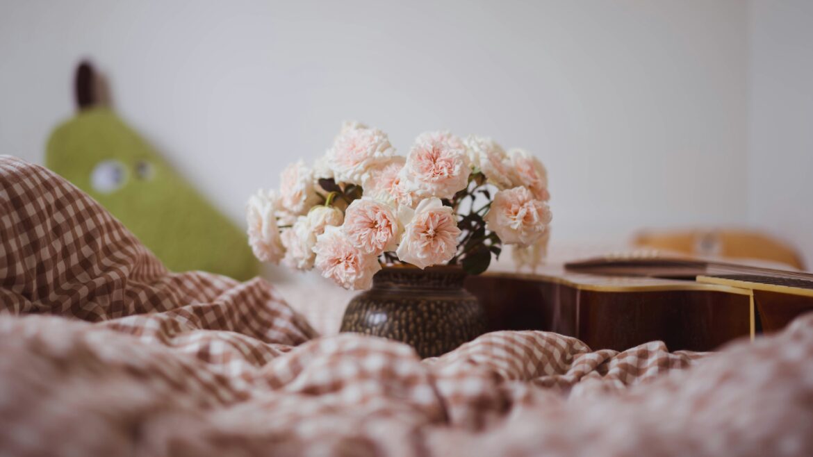 Sunlit bedside table with soft bedding, pink flowers, and a coffee cup
