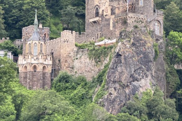 Castle Rheinstein perched on rocky cliff above the Rhine River surrounded by trees