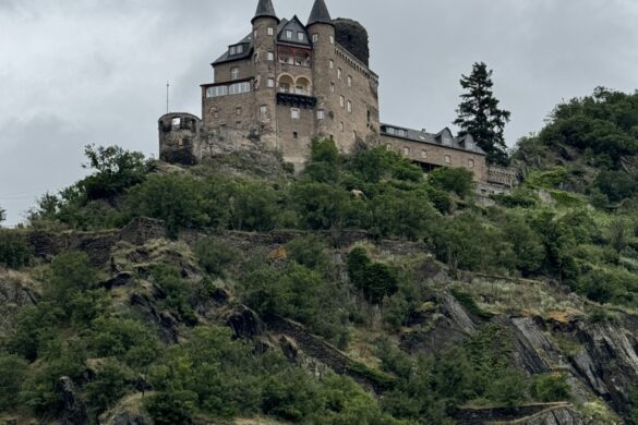Stone castle perched on rocky ridge above the Rhine River under overcast sky