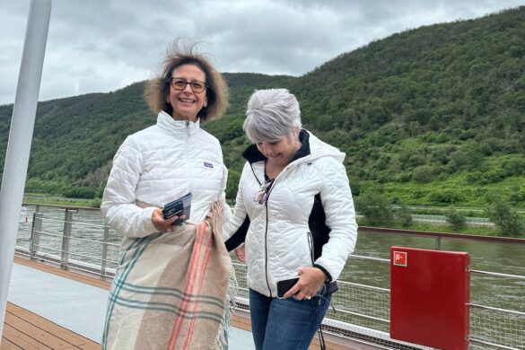 Two women standing on a river cruise deck on the Rhine River with wind blowing their hair and cloudy sky behind