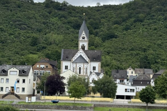White church with steeple in a small village along the Rhine River with wooded hillside behind