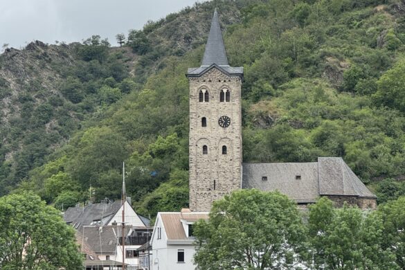 White church with tall steeple and arched bridge along the Rhine River with green hillside behind
