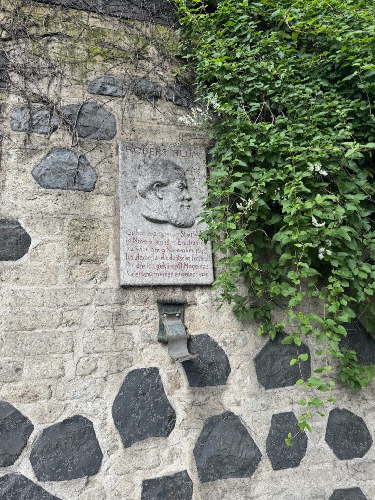 Stone memorial plaque of Robert Blum mounted on a textured stone wall with ivy growing beside it in Cologne, Germany