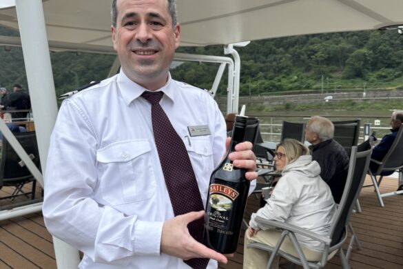 Crew member holding bottle of Bailey’s Irish Cream on cruise ship deck along the Rhine River
