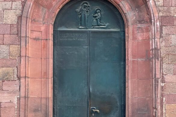tall arched bronze church door with green patina set into red sandstone Romanesque stone blocks