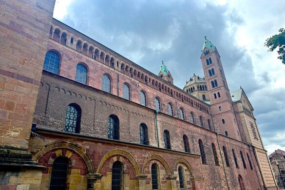 Long red sandstone façade of Speyer Cathedral stretching across the square under a cloudy sky
