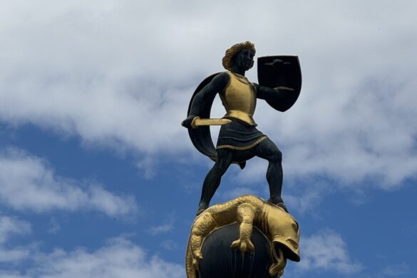 close view of bronze and gold statue of Saint George holding a shield and sword standing on a dragon against a cloudy sky