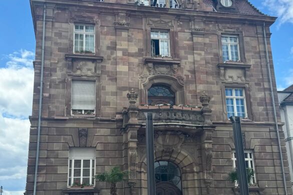 tall historic stone civic building with ornate baroque gable roofline and arched doorway under blue sky