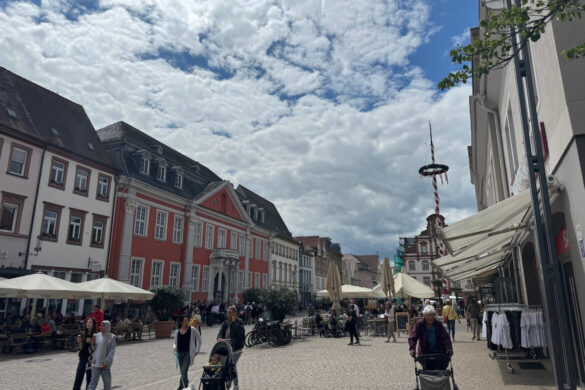 pedestrian street with pastel historic buildings outdoor cafes and people walking under a partly cloudy sky
