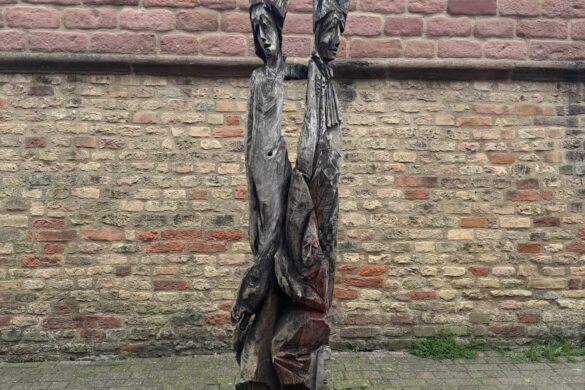 abstract carved wooden sculpture standing in front of an old stone and brick wall