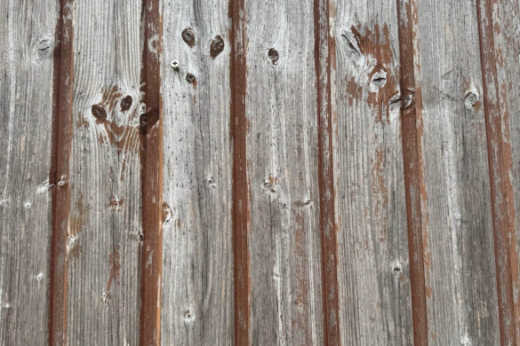 close up of vertical weathered wooden boards with peeling paint and visible grain and knots