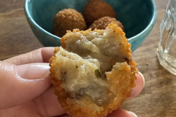 hand holding a bitten bitterbal showing creamy beef ragout filling inside crispy coating