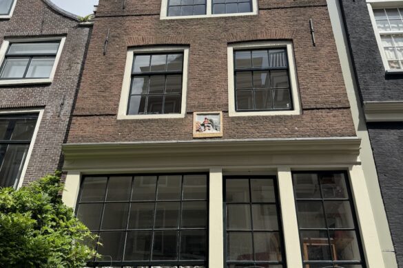 tall narrow amsterdam canal house with a decorative gevelsteen plaque centered on the facade