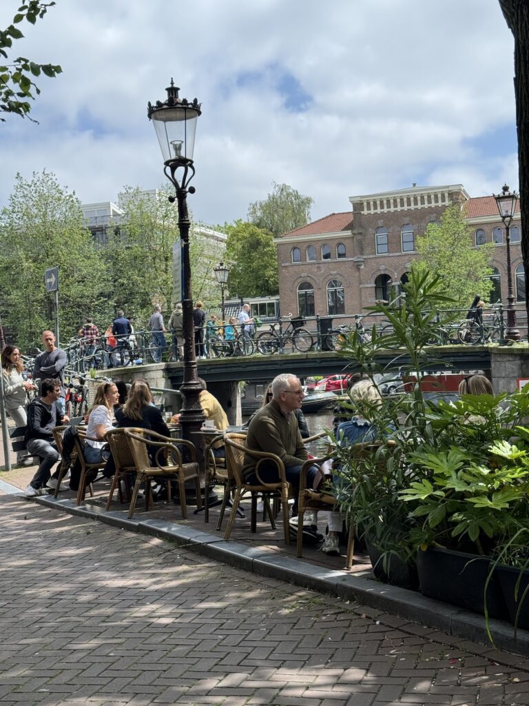 outdoor canal-side cafe in Amsterdam with people seated at tables on a sunny spring day