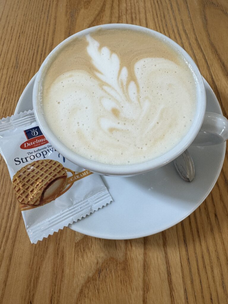 cappuccino with latte art on a white saucer with a wrapped stroopwafel on a wooden table in amsterdam
