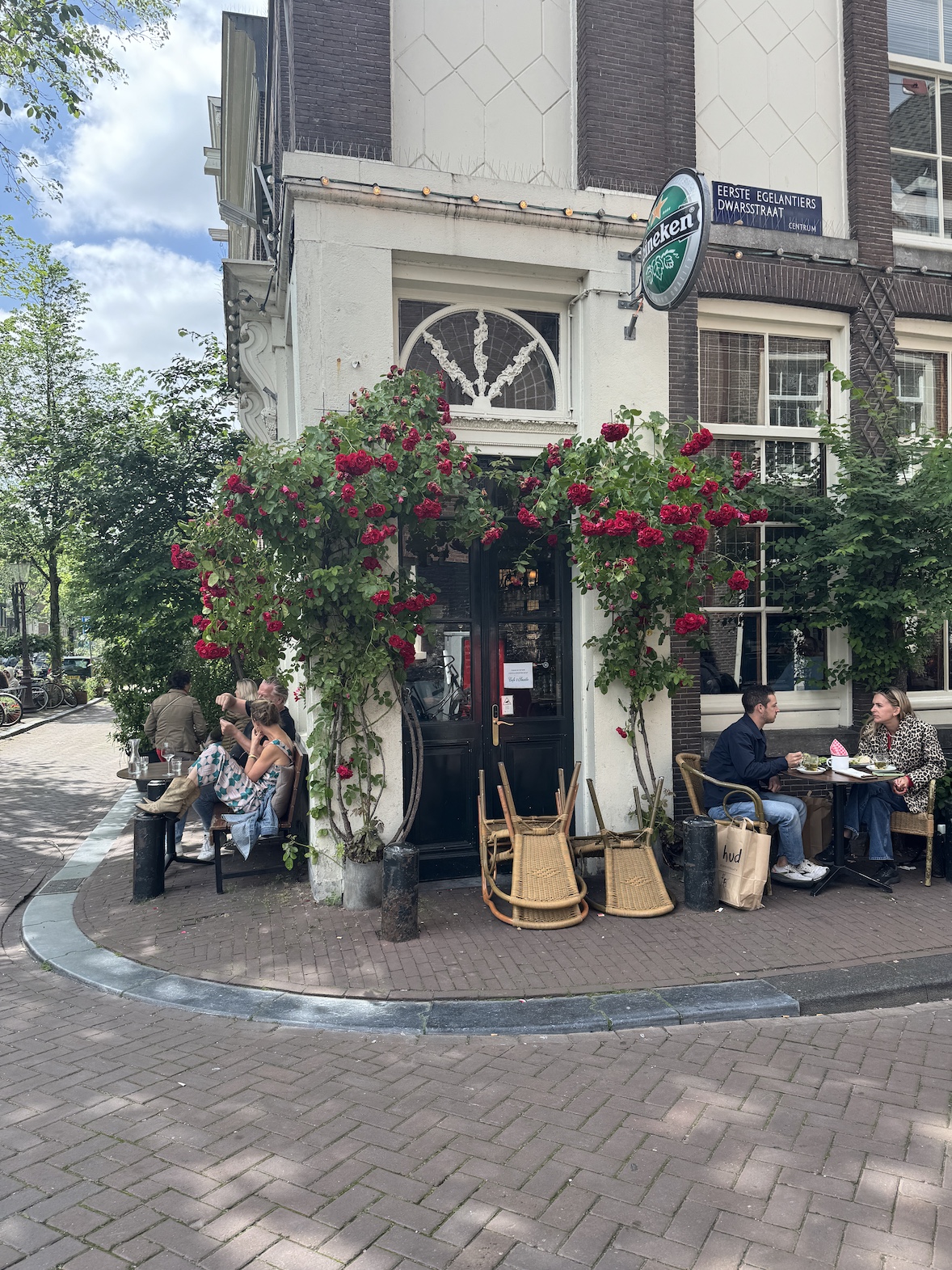 corner cafe in amsterdam with outdoor seating, red flowers, and people sitting at small tables