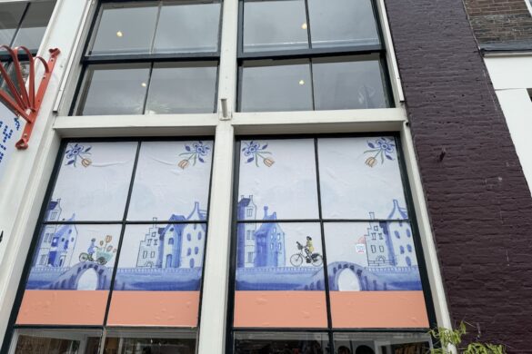 Amsterdam storefront window decorated with Delft-blue style illustrated buildings and floral motifs