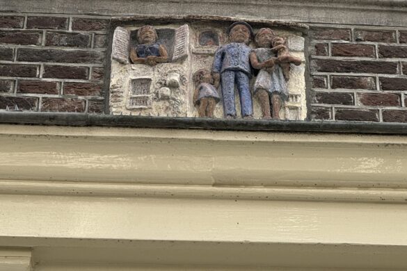 close-up of a gevelsteen relief showing small carved figures set into a brick building facade in amsterdam