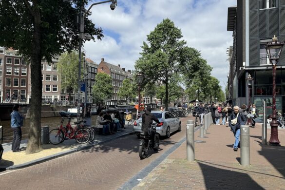 amsterdam street scene with canal, bicycles, pedestrians, and anne frank house entrance on the right