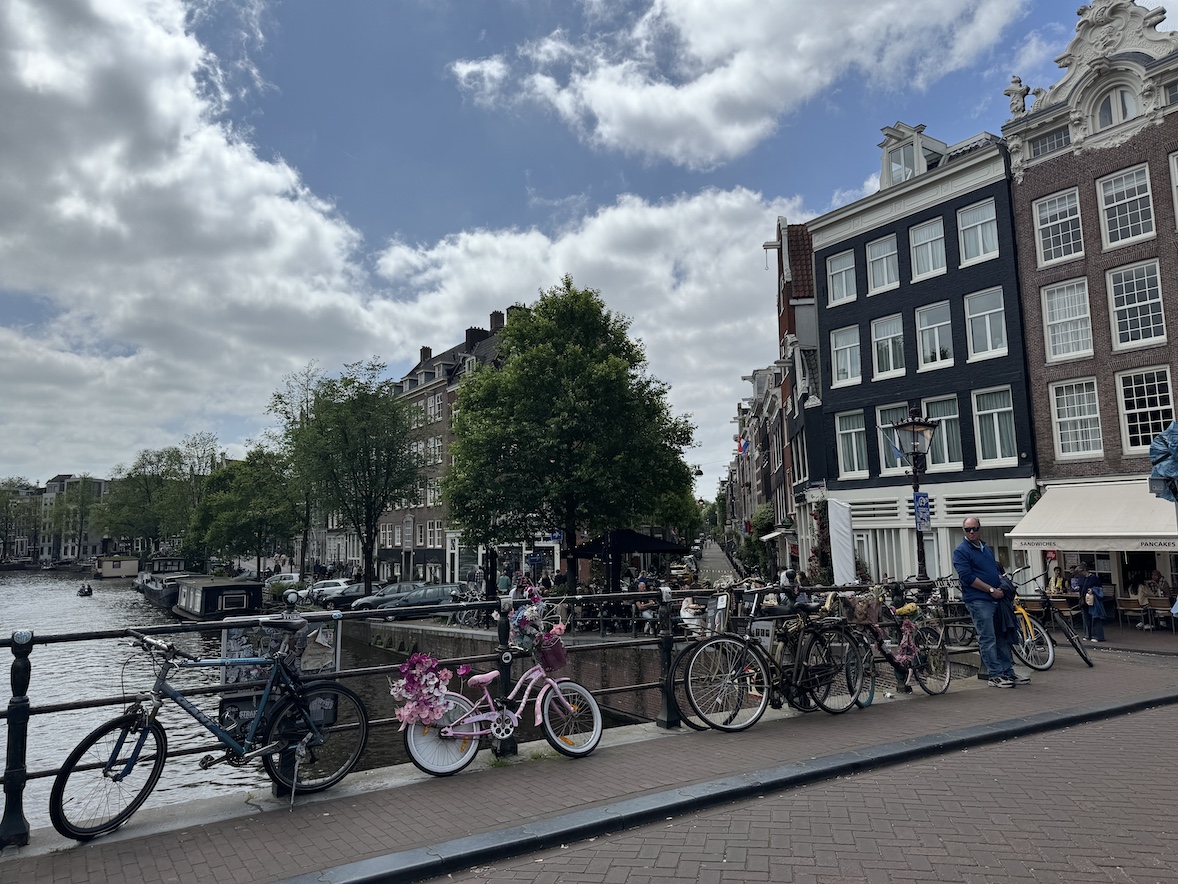 amsterdam canal street with rows of parked bicycles along a bridge and traditional narrow buildings