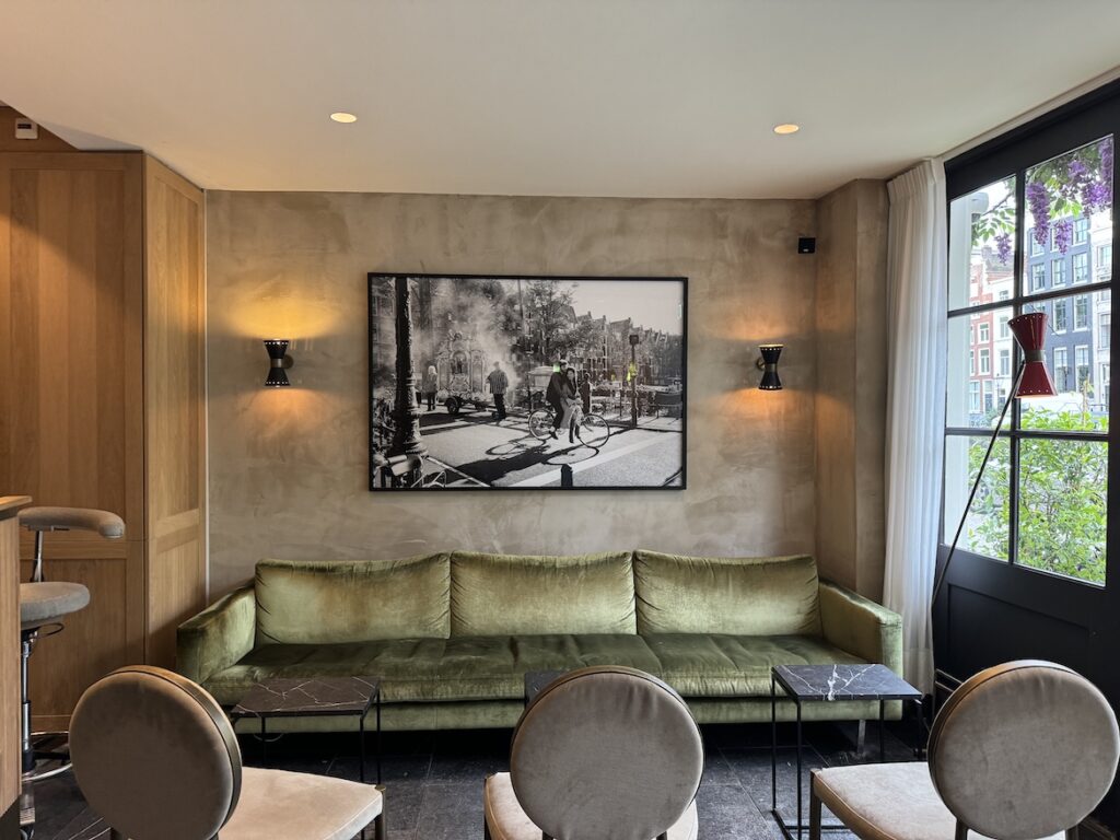 Green velvet sofa in The Times Hotel lobby in Amsterdam with black-and-white street photograph and canal houses visible through the window