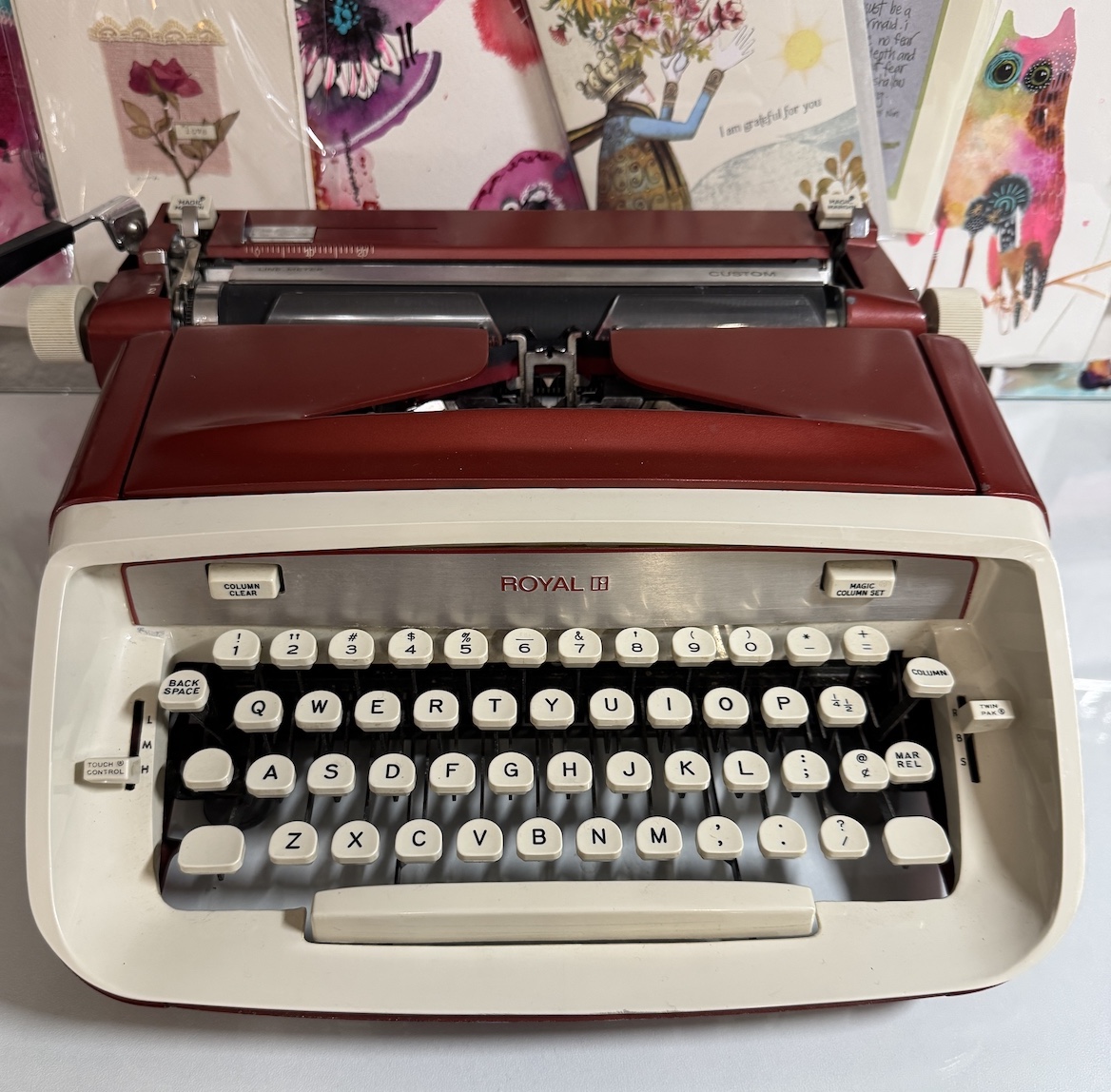 vintage red Royal typewriter on desk with art and writing materials behind it