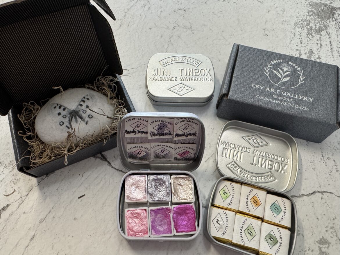 metallic watercolor paint tins in small travel cases with shimmering colors displayed