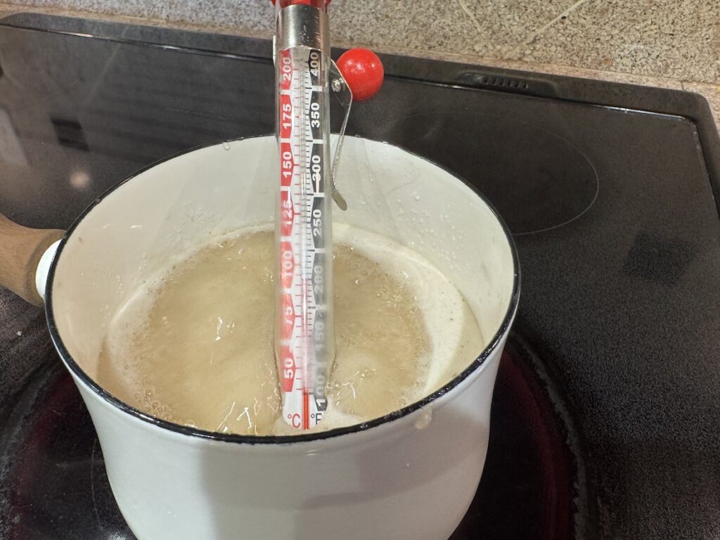 Candy thermometer in saucepan heating sugar and corn syrup mixture for marshmallows