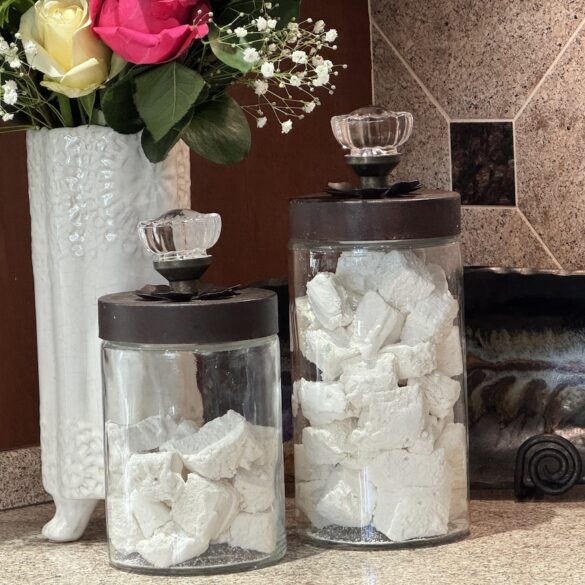 Homemade marshmallows in glass jars on a kitchen counter with flowers in the background