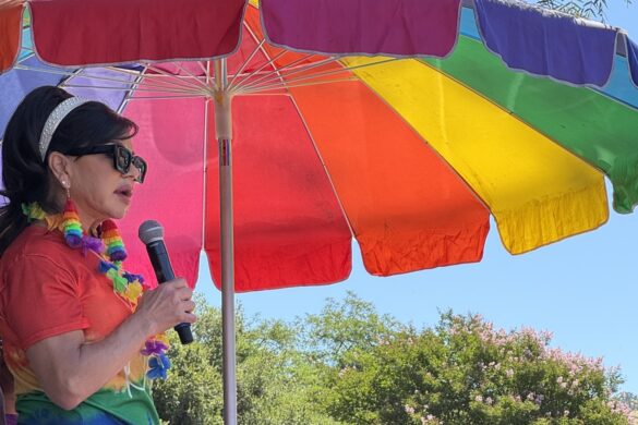 KTVU meteorologist Roberta Gonzales speaking as Grand Marshal of the Clayton Pride Parade beneath a rainbow umbrella