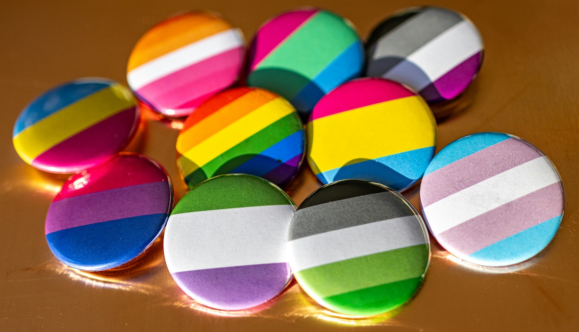 Collection of pride flag buttons representing different LGBTQIA+ identities arranged on a table