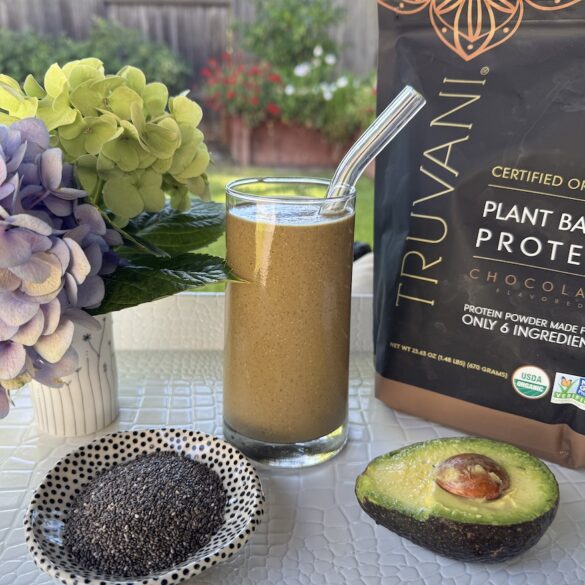 Deborah's Velvet Green Smoothie in a glass beside Truvani Chocolate Protein powder, topped with kiwi and chia seeds.