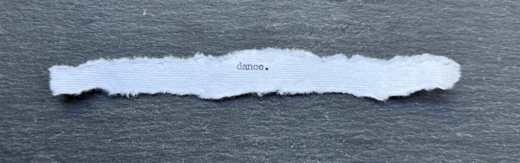 Torn typewritten note reading “Dance.” on black stone