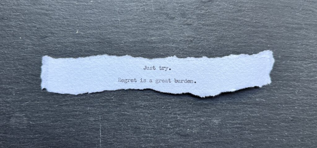 Torn typewritten note reading “Just try. Regret is a great burden.” on black stone