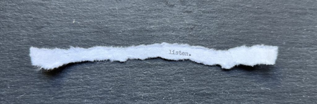 Torn typewritten note reading “Listen.” on black stone