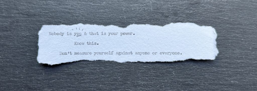 Torn typewritten note reading “Nobody is you and that is your power” on black stone
