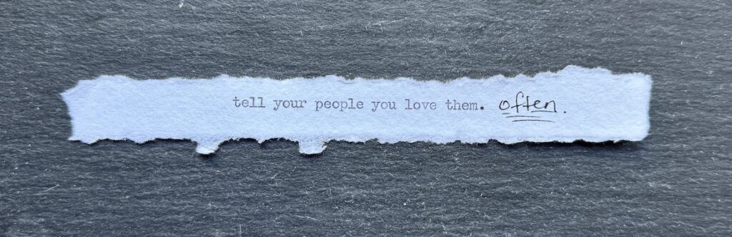 Torn typewritten note reading “Tell your people you love them. Often.” on black stone